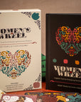 Two 'Women's Wheel' books with colorful designs on a wooden surface.