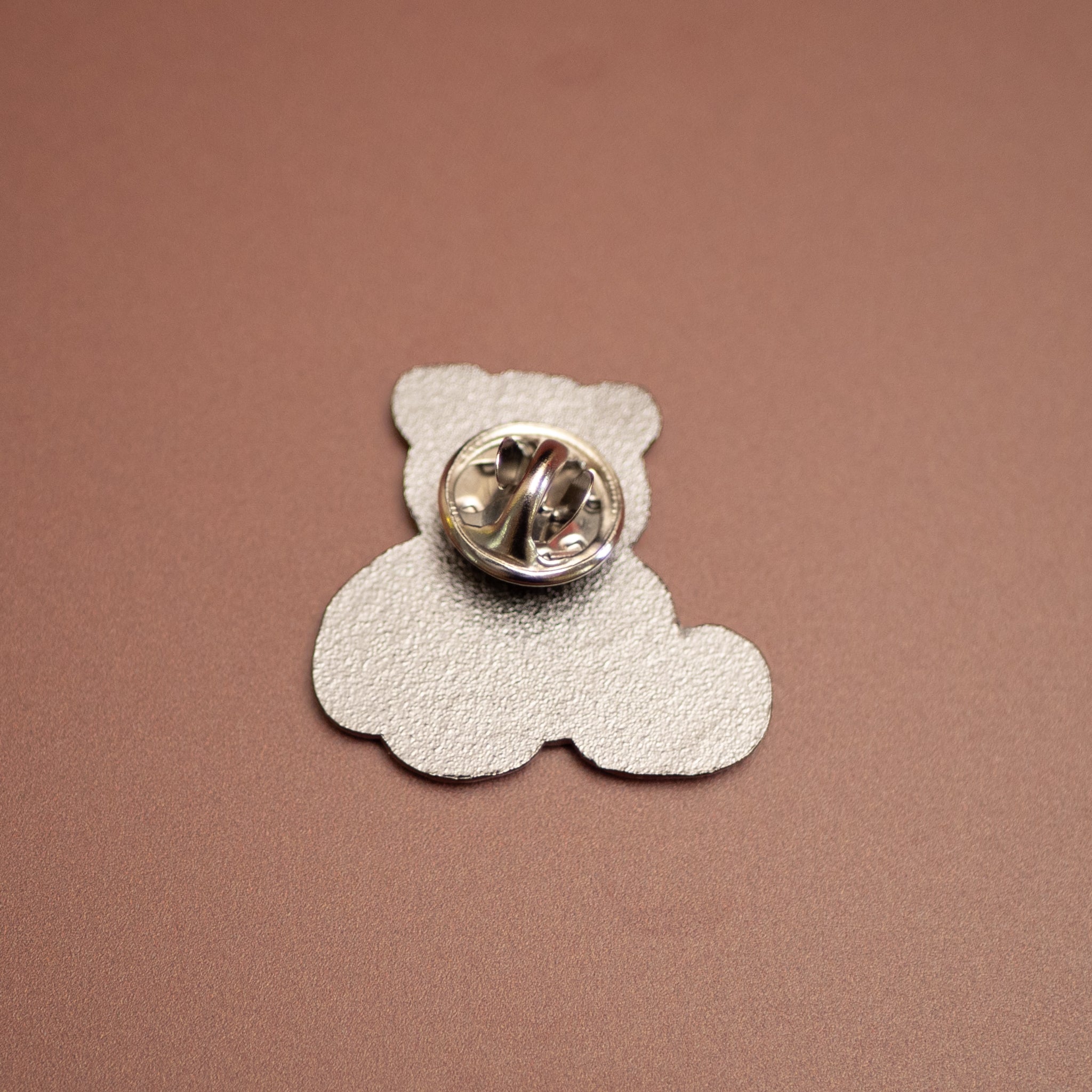 Silver teddy bear-shaped pin on a brown background