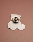 Silver teddy bear-shaped pin on a brown background