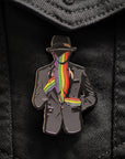 Pin with a design of a person wearing a suit and hat with a rainbow scarf on a black denim background