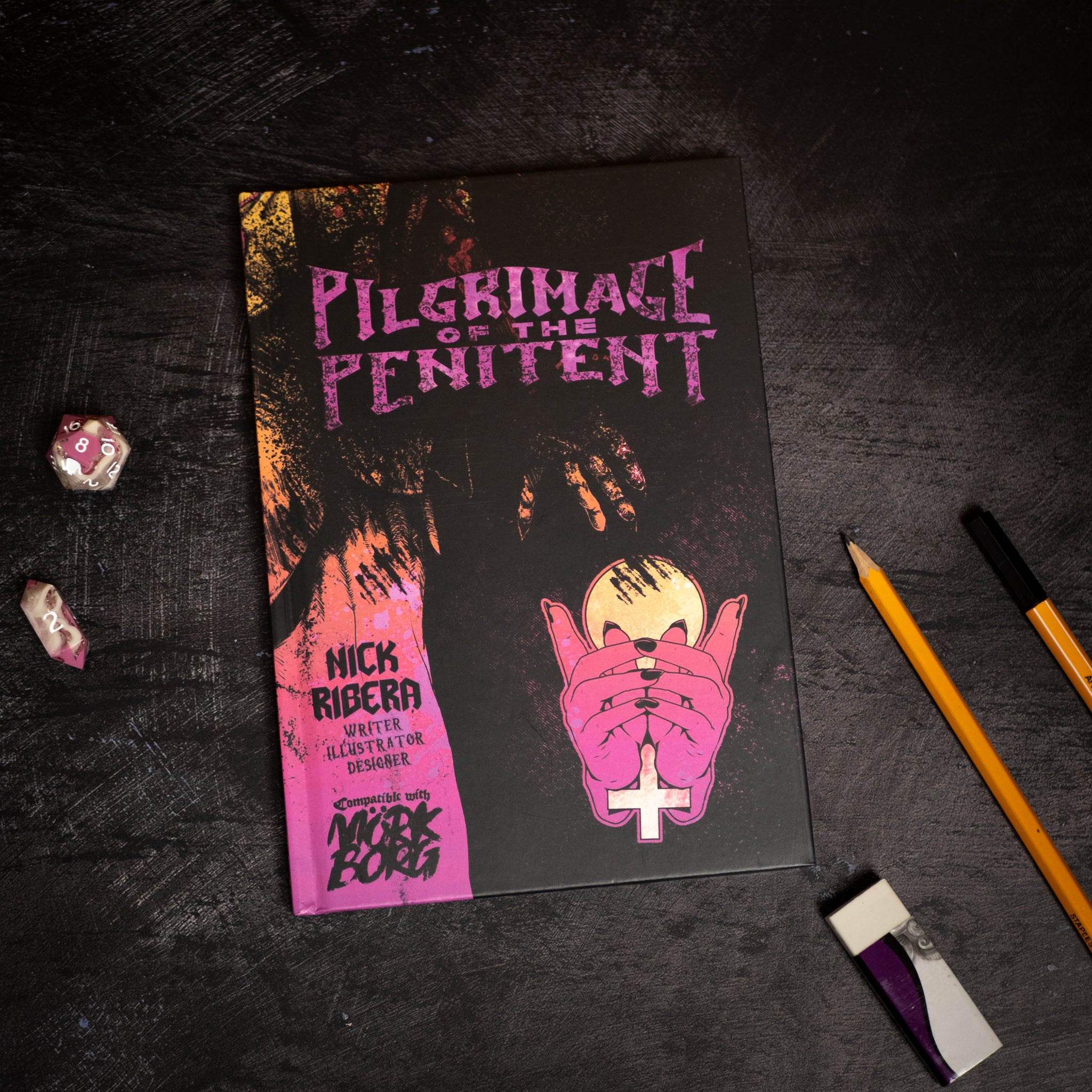 Book titled 'Pilgrimage of the Penitent' on a dark surface with pencils and crystals.