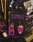 Book titled 'Pilgrimage of the Penitent' with artwork on a dark surface