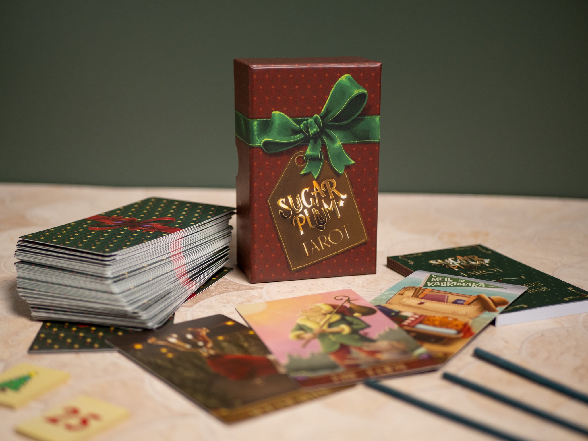 Card game with a red box featuring a green bow and 'A Sugar Plum Carol' text on a wooden surface.