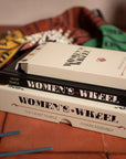 Stack of books titled 'Women's Wheel' on a textured surface with a blurred background